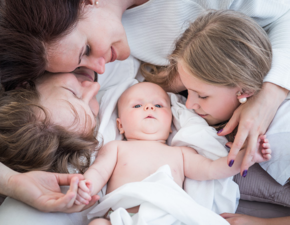 two women and two girls smiling and interacting with a baby lying on a blanket family bonding joyful moments love and connection with eight important values