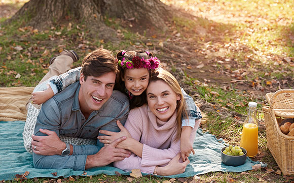 happy family enjoying picnic outdoors with child wearing flower crown surrounded by nature relaxing on blanket three generations together