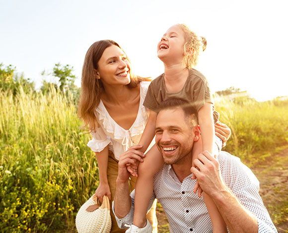 happy family enjoying a sunny day outdoors with a young girl laughing while sitting on her father's shoulders in a grassy field celebrating joyful moments and experiences together five times