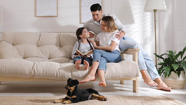 a family of three sitting together on a couch with a dog beside them the father is holding the mother and the daughter is reading a book capturing a cozy family moment in a bright living room with eight happy moments