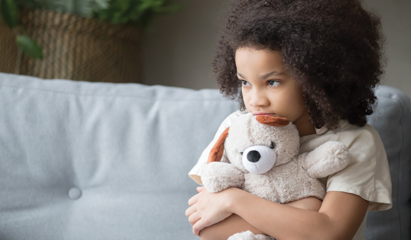 young girl sitting on gray sofa holding stuffed dog looking sad emotional moment 7 comforting toys