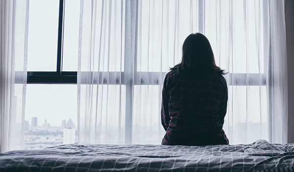 woman sitting on bed looking out of window through sheer curtains with a city view reflecting a moment of contemplation and solitude in her life at eleven