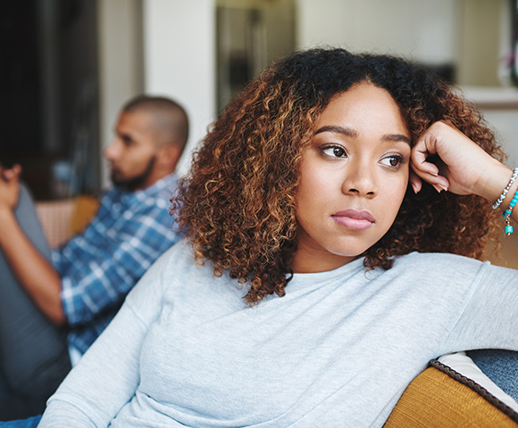 thoughtful woman sitting on sofa looking away with man in background appearing distracted showing emotional distance and relationship tension in intimate setting 5 ways to improve communication
