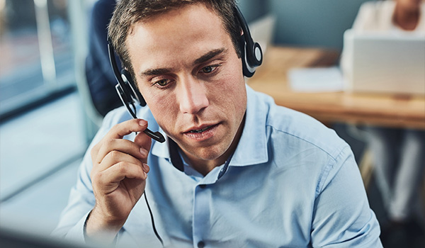 man wearing a headset focused on a computer screen in an office environment giving customer support in a busy workspace 9 effective communication skills