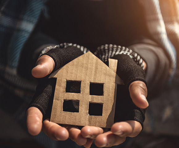 person holding cardboard house model in their hands representing home and shelter importance in community supporting 5 initiatives