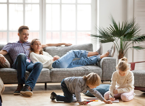 family playing together in cozy living room with children drawing and parents relaxing while enjoying quality time at home